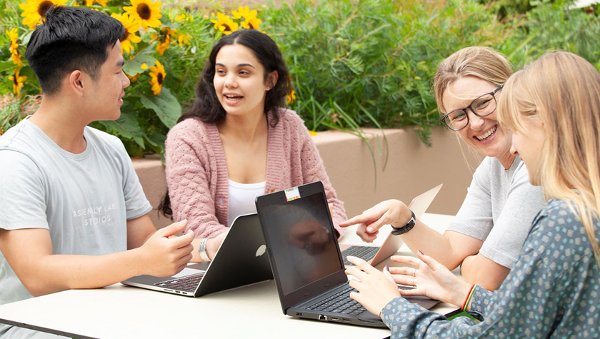 Schülerinnen und Schüler der Deutschen Internationalen Schule Sydney sitzen mit Laptops an einem Tisch und diskutieren