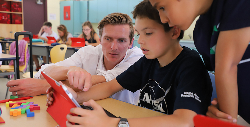 Ein Lehrer schaut gemeinsam mit zwei Schülern auf ein Tablet