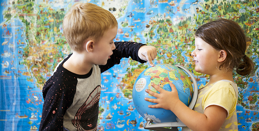 Eine Schülerin und ein Schüler mit einem Globus vor einer Weltkarte